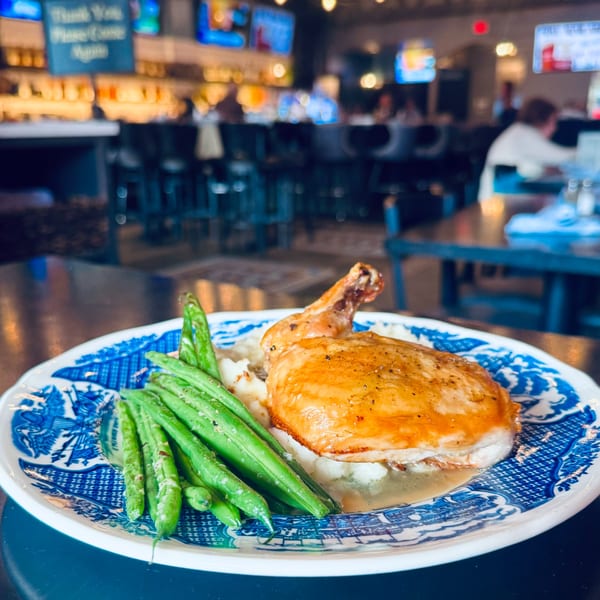 Roasted chicken leg with mashed potatoes and green beans on a blue and white plate at Label Kitchen + Bar.