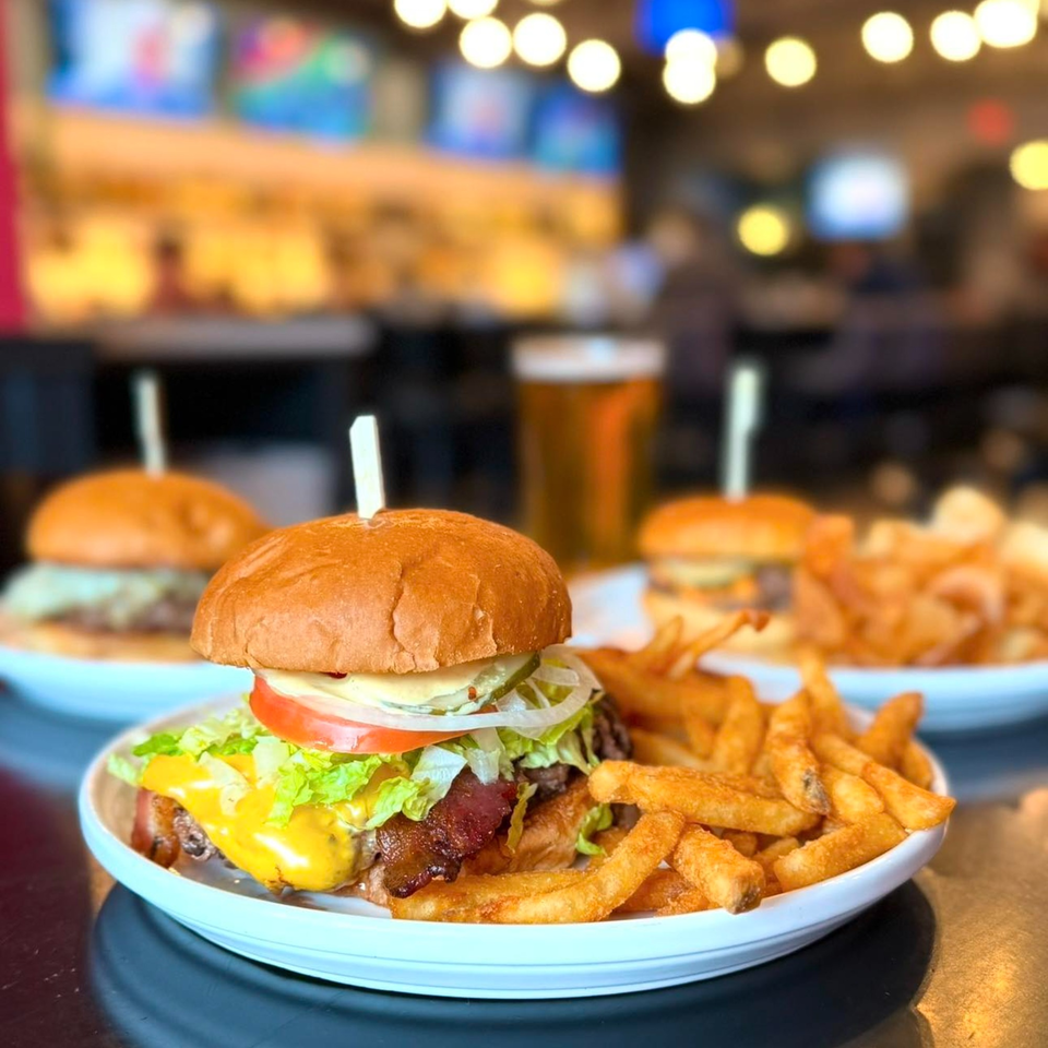 A Label Kitchen + Bar cheeseburger with fries, with another burger and beer in the background.