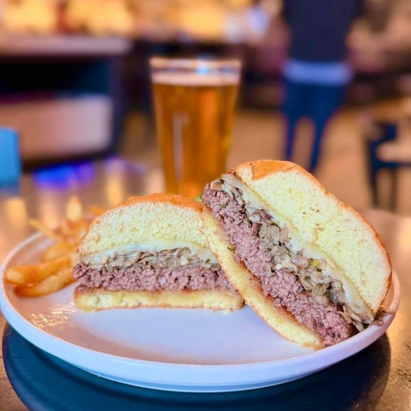 A Label Kitchen + Bar burger, cut in half, with fries and a beer in the background.