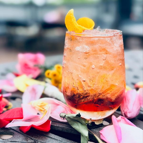 A refreshing Label Kitchen + Bar cocktail with orange peel, surrounded by pink and yellow flower petals.