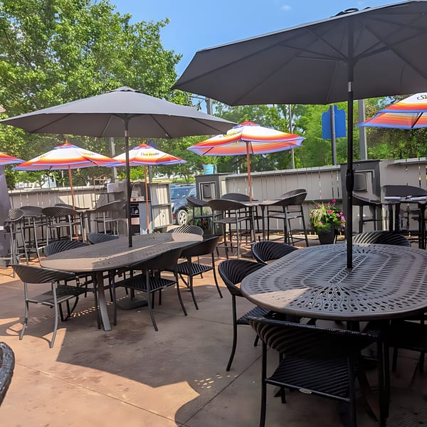 Outdoor patio at Label Kitchen + Bar with black tables, chairs, and umbrellas under a blue sky.