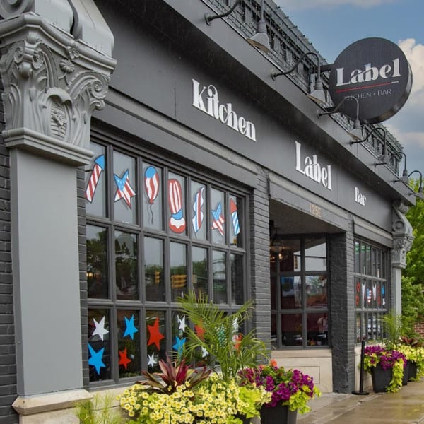 Exterior of Label Kitchen + Bar, a dark brick building with patriotic window decorations and flower planters.