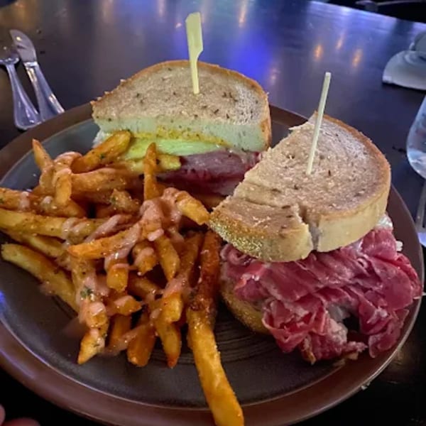 Two corned beef sandwiches on rye with a side of seasoned fries drizzled with sauce.