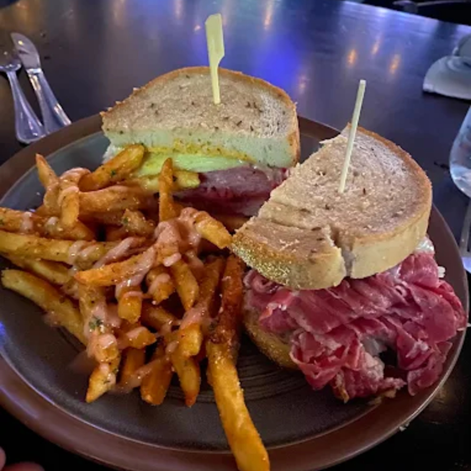 Two corned beef sandwiches on rye with a side of seasoned fries drizzled with sauce.