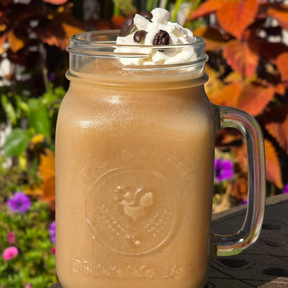 A frozen coffee drink with whipped cream and coffee beans in a mason jar, outdoors.