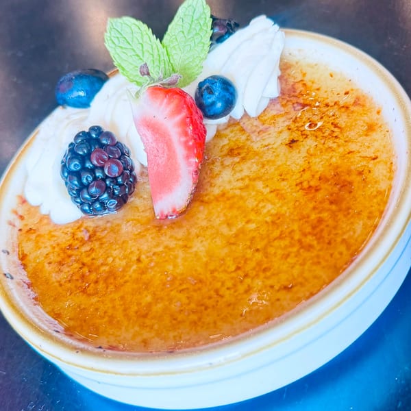 Crème brûlée topped with whipped cream, a strawberry slice, blackberries, blueberries, and mint.