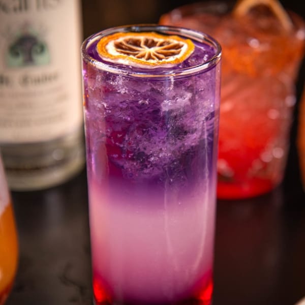 A vibrant purple and pink cocktail with a dried orange slice garnish, from Label Kitchen + Bar.