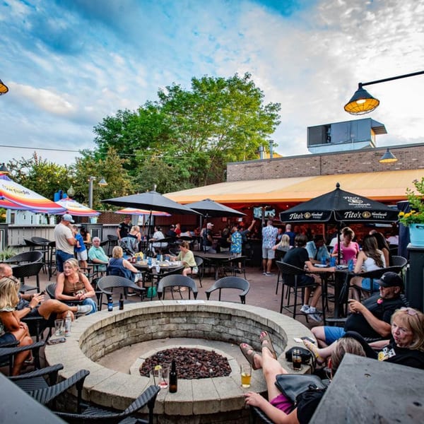 Patrons enjoying drinks and conversation on the Label Kitchen + Bar outdoor patio with a fire pit.