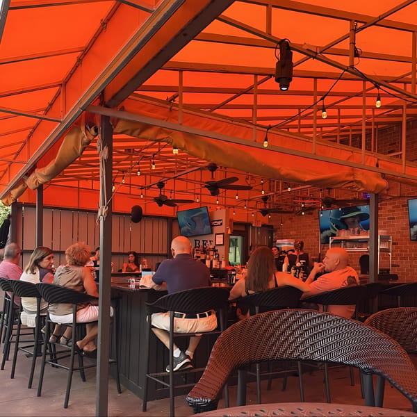 Patrons seated at the outdoor bar of Label Kitchen + Bar under a bright orange awning.