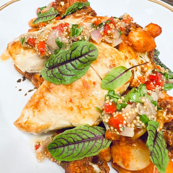 Close-up of Label Kitchen + Bar's chicken dish, garnished with red peppers, mustard seeds, and sorrel leaves.