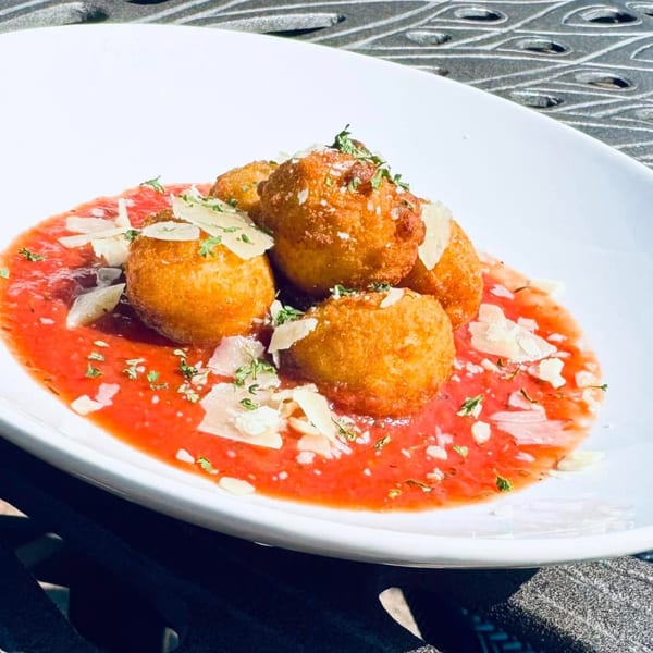 Golden-fried arancini balls in a vibrant red sauce, garnished with parmesan and fresh herbs.
