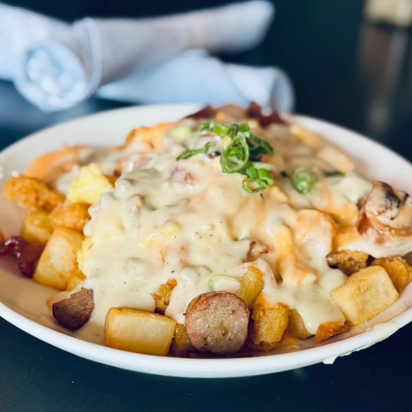 A breakfast poutine with crispy potatoes, scrambled eggs, sausage, gravy, and melted cheese.