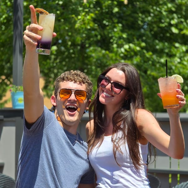 Two smiling people, a man and a woman, holding up cocktails at Label Kitchen + Bar.