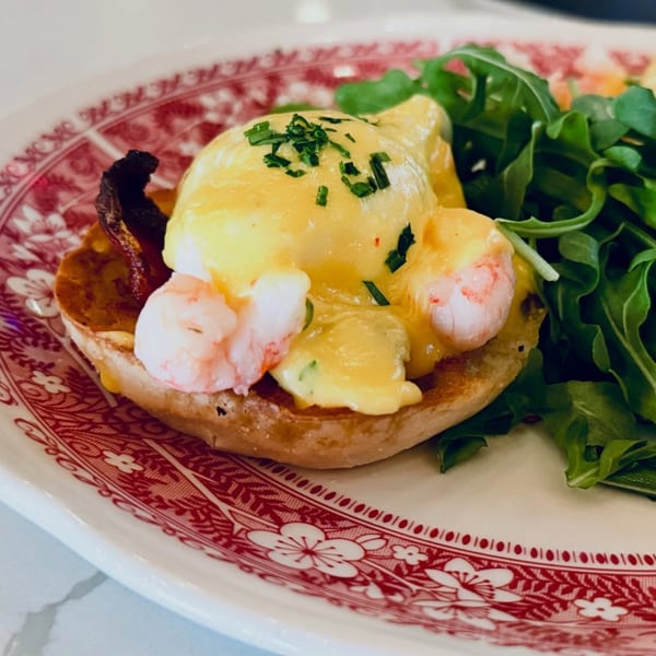 Shrimp Eggs Benedict with hollandaise sauce and chives, served with a side of arugula on a patterned plate.